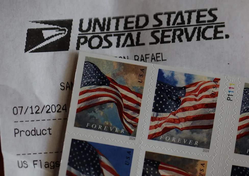 Un employé de l'USPS triant des lettres à côté de timbres Forever aux États-Unis.